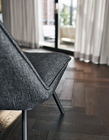 Drewniana podłoga, nowoczesny fotel na oknie szare zasłony